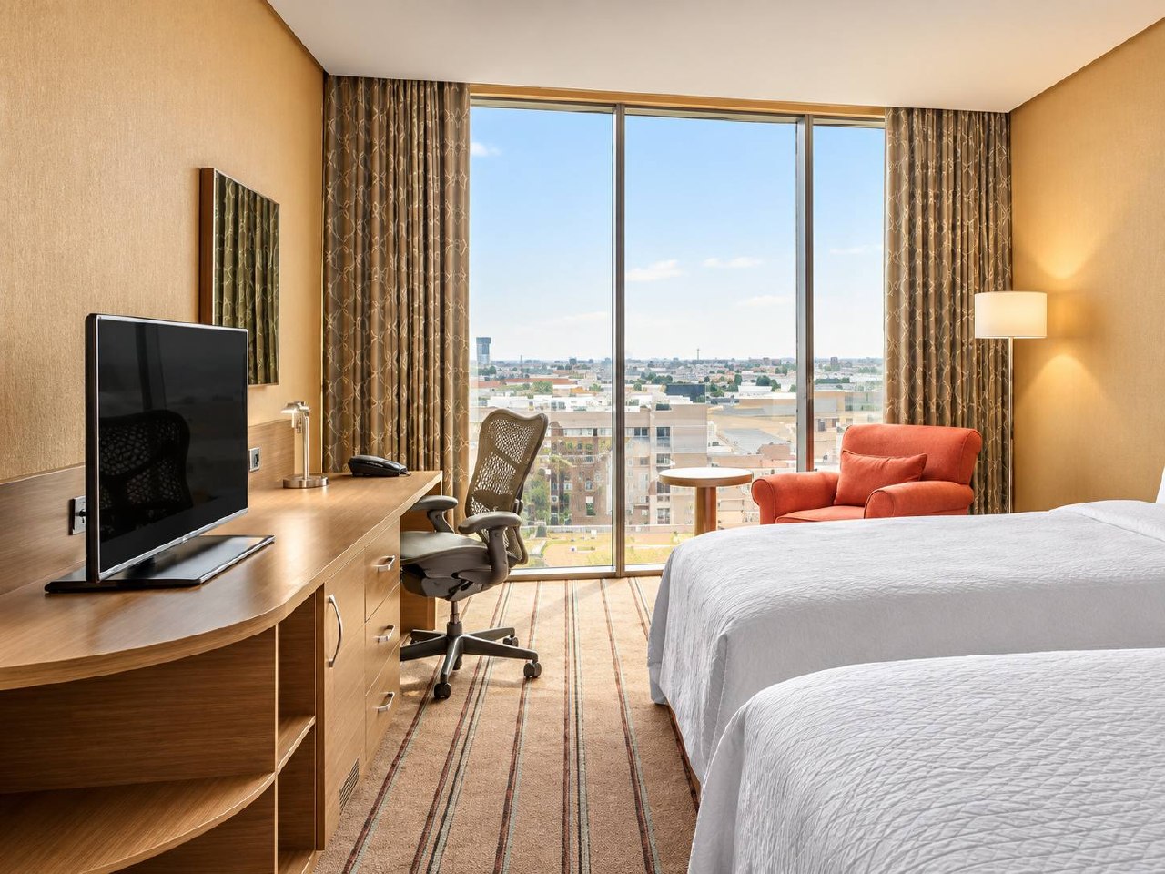 Guest room with desk, television and city view through a large window